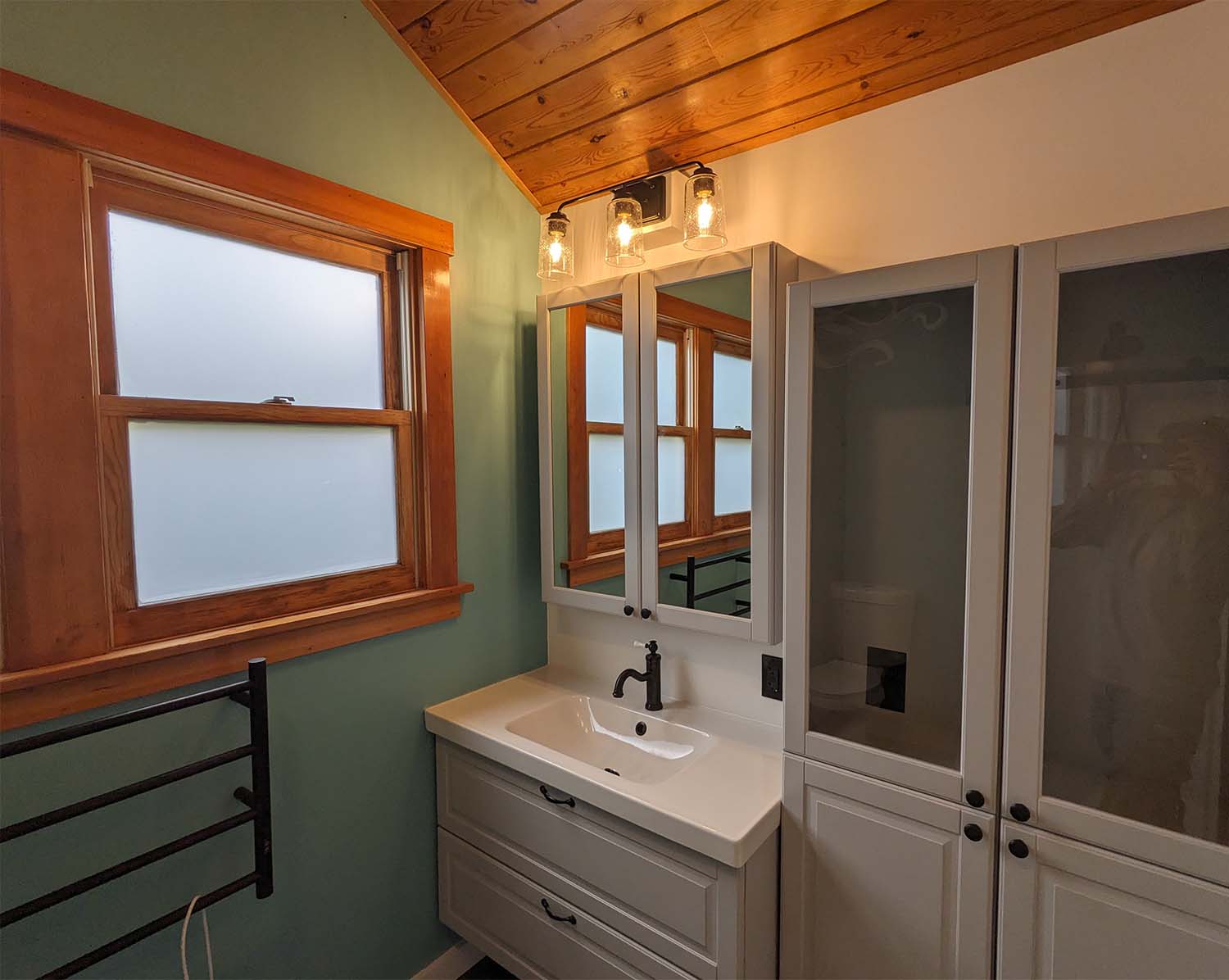 A photo of a well-lit bathroom sink, cabinet, and window. There is a lot of natural wood in the design.