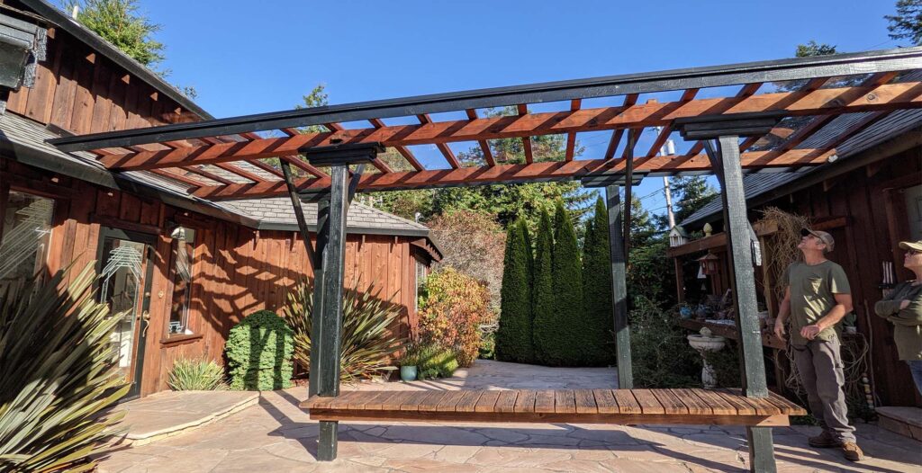 Two people stand looking up at a beautiful glass and stained wood pergola