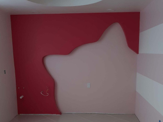 An interior photo of a well-designed room. The walls are painted light pink, and one wall has a large dark red cutout of a cat on it. The ceiling has a large inset circle for lighting