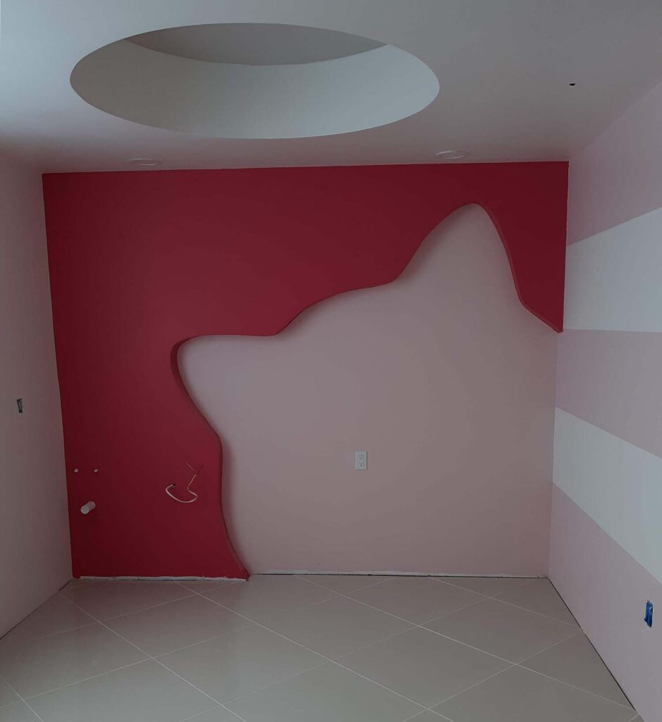 An interior photo of a well-designed room. The walls are painted light pink, and one wall has a large dark red cutout of a cat on it. The ceiling has a large inset circle for lighting