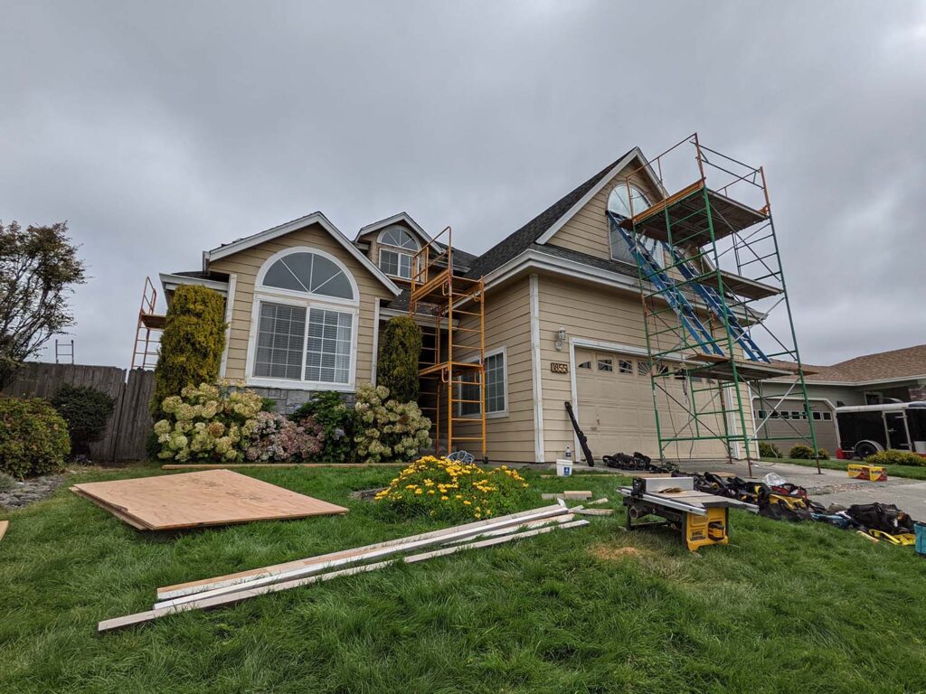 A low shot of a house exterior. There is scaffolding up the front of the house and tools and materials in the yard.