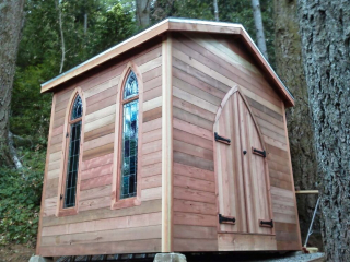 A cabin in the forest with raw wood siding.