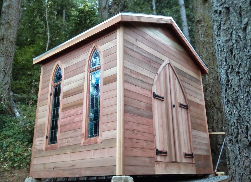 A cabin in the forest with raw wood siding.