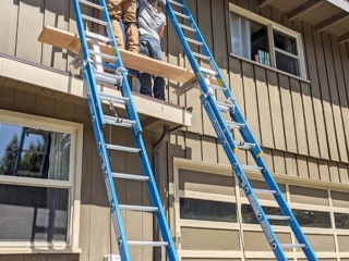 Two people work on scaffolding on the second story of townhouse-style apartments